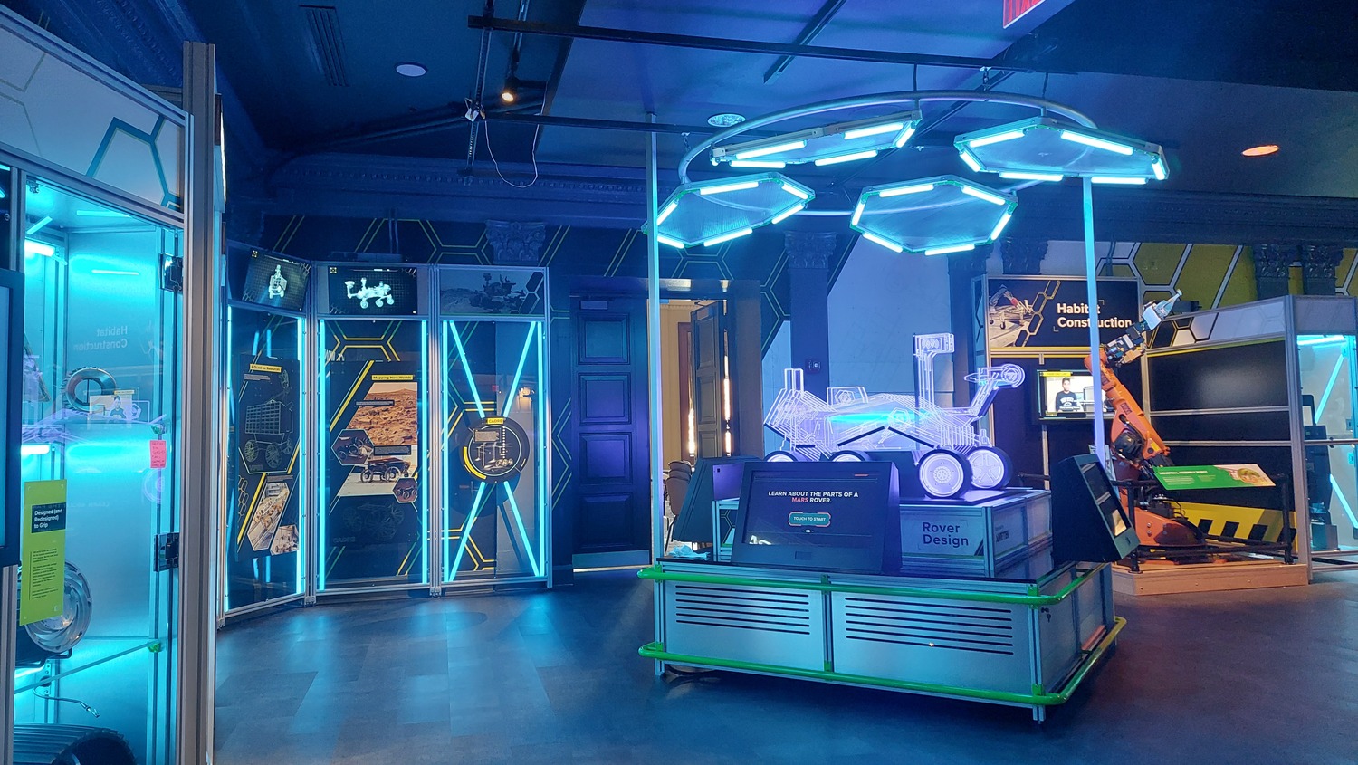 Salle d'exposition dotée d'un éclairage bleu futuriste, d'une maquette de rover intitulée 