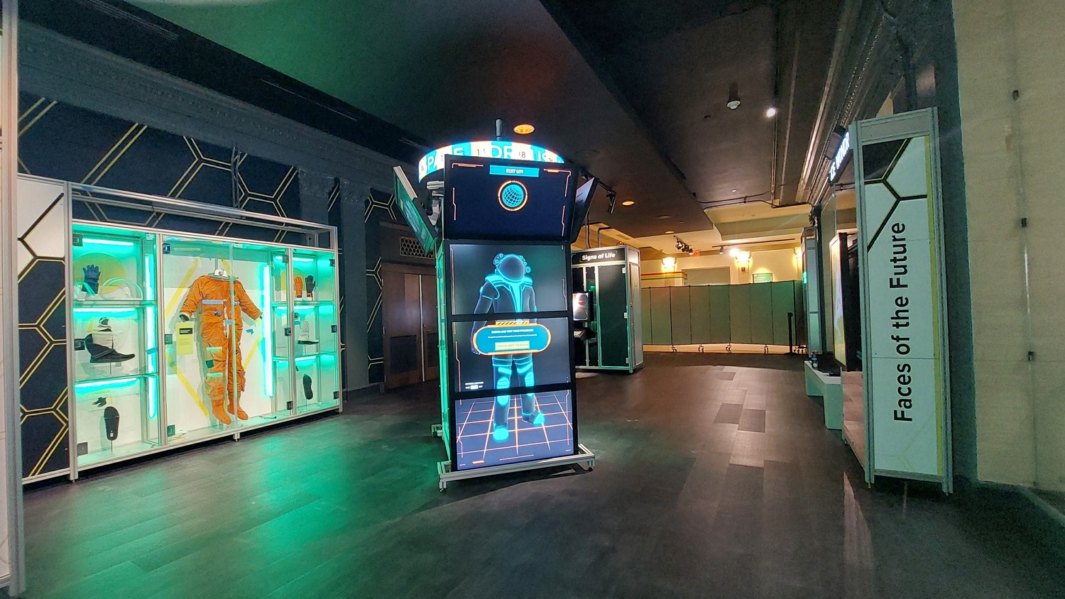 Une exposition moderne présente une combinaison d'astronaute, un écran numérique interactif avec une silhouette humaine et un panneau indiquant 