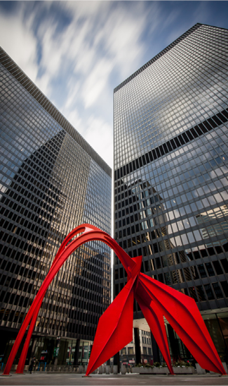 A red sculpture in front of tall buildings.