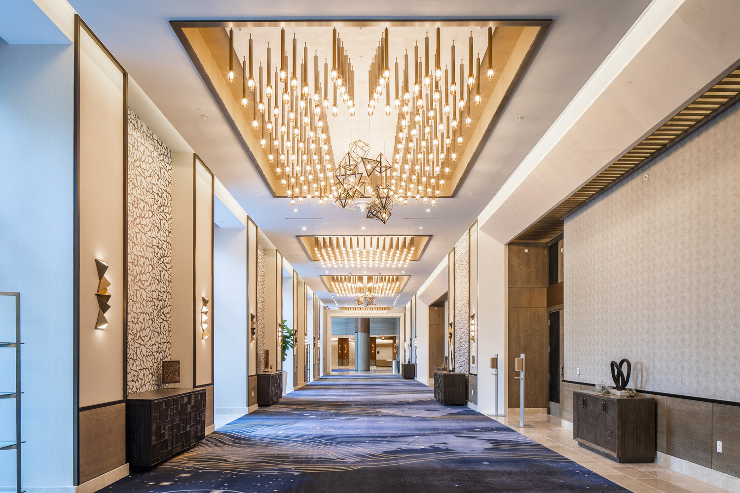 A hallway in a hotel with a chandelier and blue carpet.