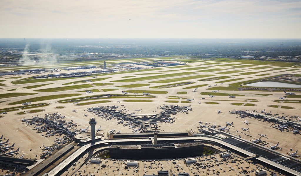 Aerial view of a busy airport with multiple runways and taxiways, showcasing aircraft at gates and in motion.