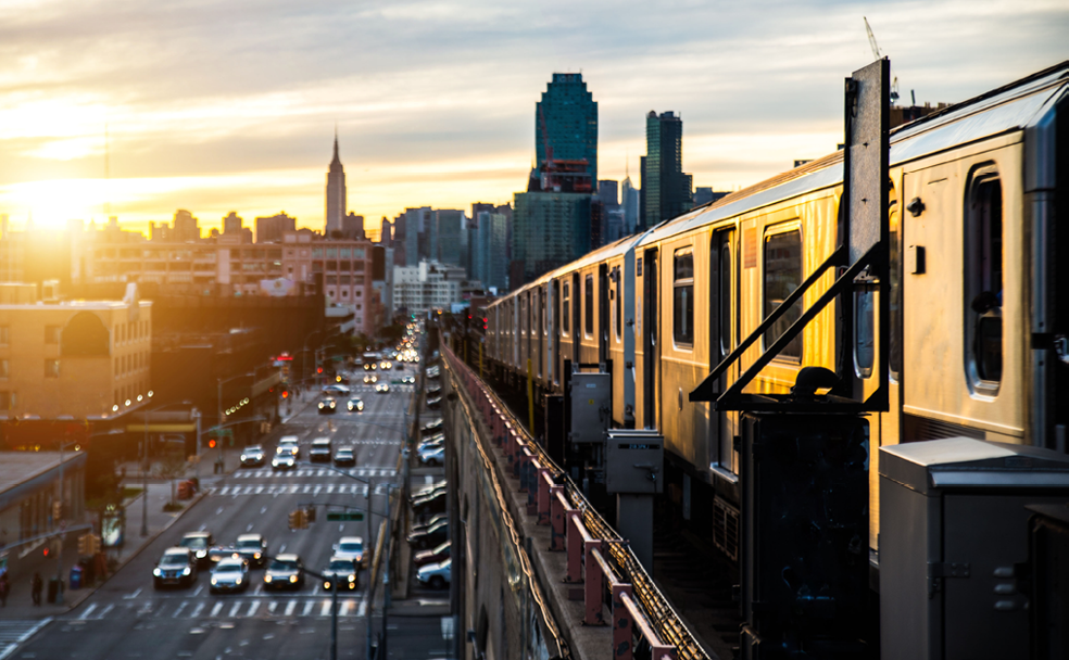 Sunset over an urban cityscape with a train moving along an elevated track.