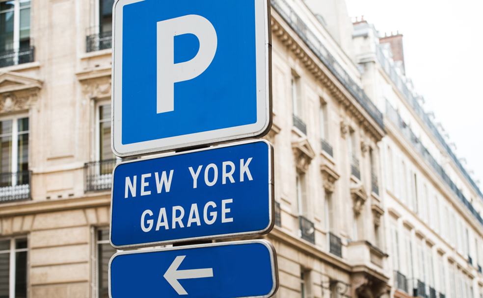 Parking and new york garage direction signs with an arrow on a city street.