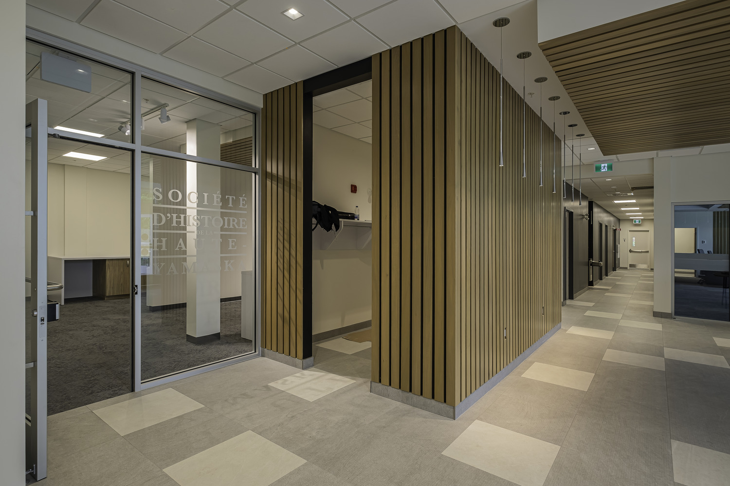 Couloir de bureau moderne avec portes vitrées, murs à lattes de bois et carrelage à motifs.