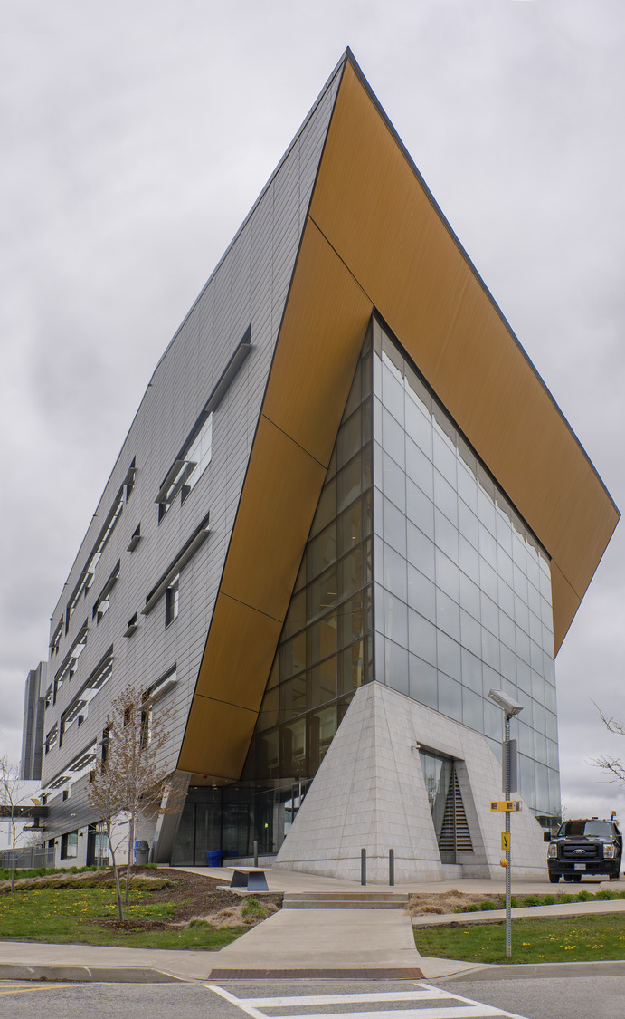 Modern architectural building with a sharp triangular overhang and a mix of glass and metallic facades under overcast skies.