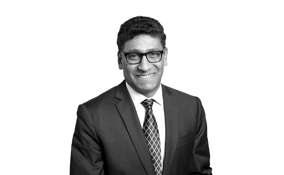 A man in a suit and tie smiling at the camera in a black and white photograph.