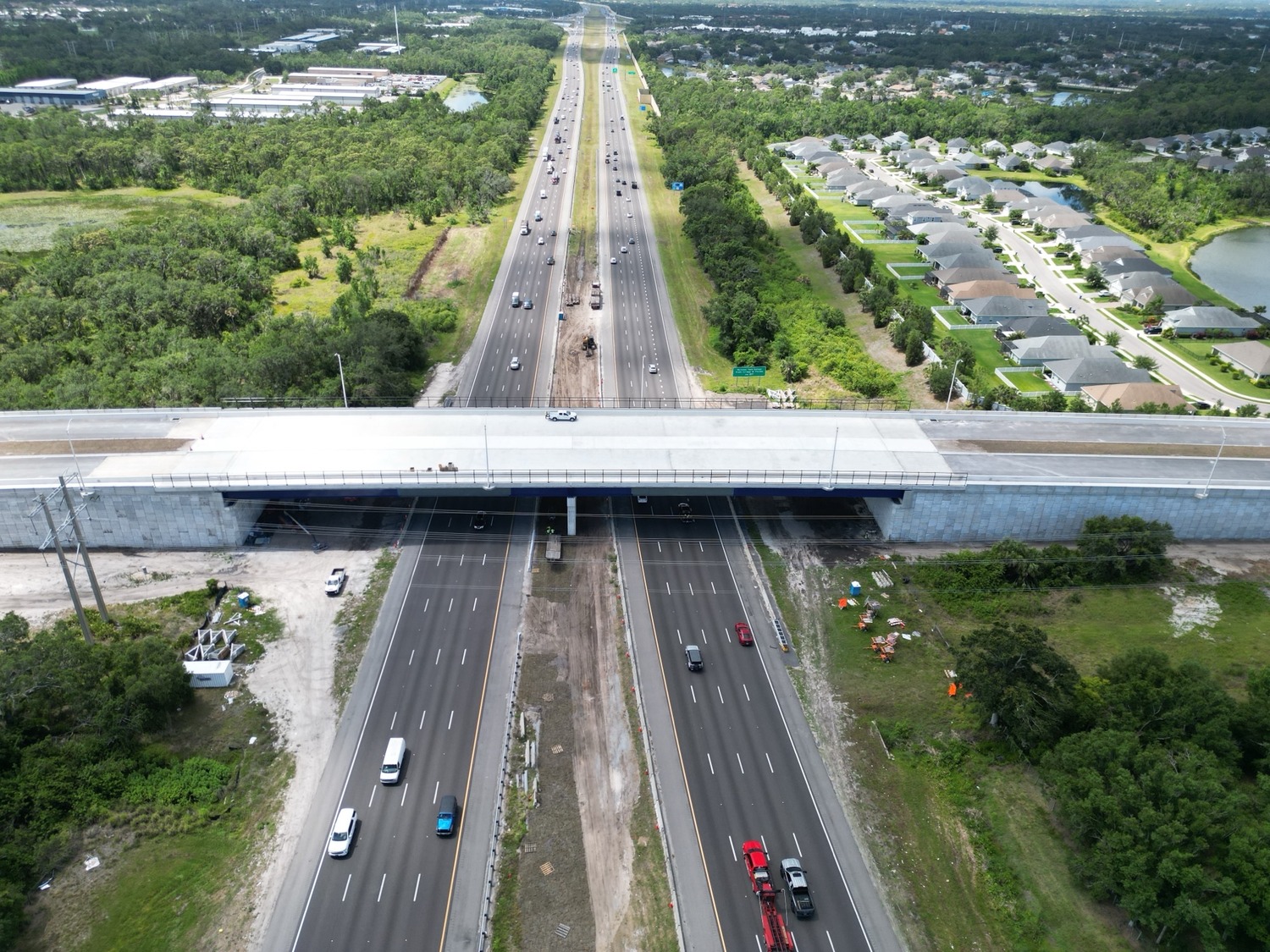 Vue aérienne d'un viaduc routier à plusieurs voies de circulation dans les deux sens, entouré d'arbres et de maisons résidentielles.