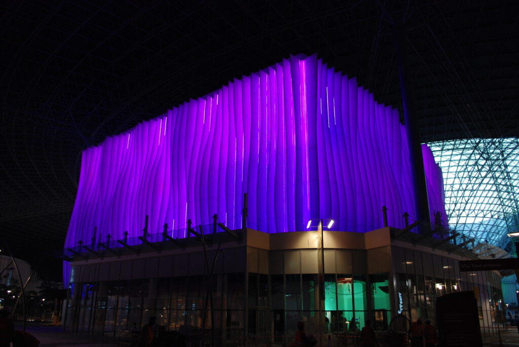 A modern building with vertical purple lights and a glass façade, illuminated at night.