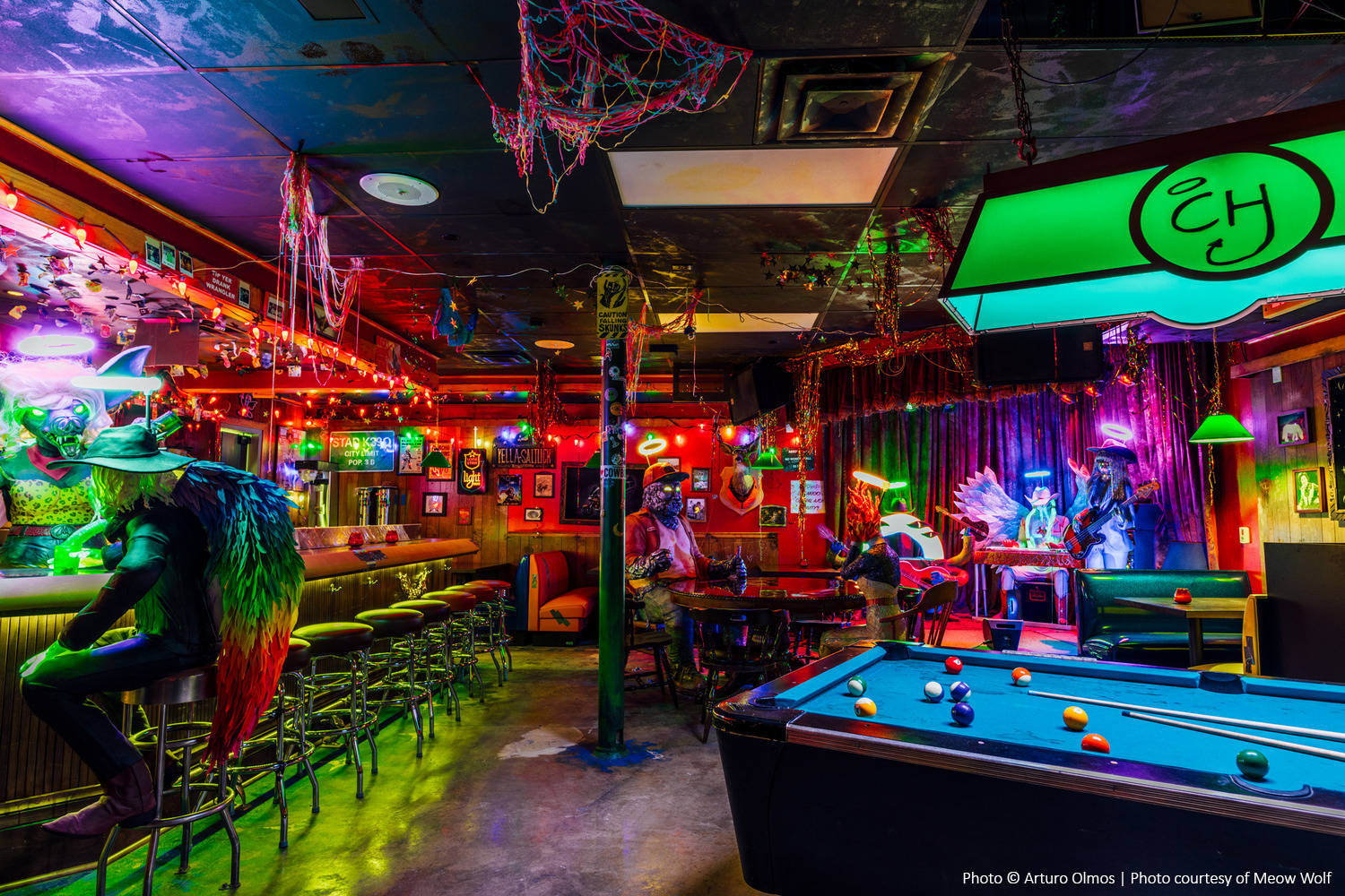 L'intérieur du bar coloré et éclectique comprend une table de billard, des mannequins en costumes, des guirlandes lumineuses et un décor vibrant.