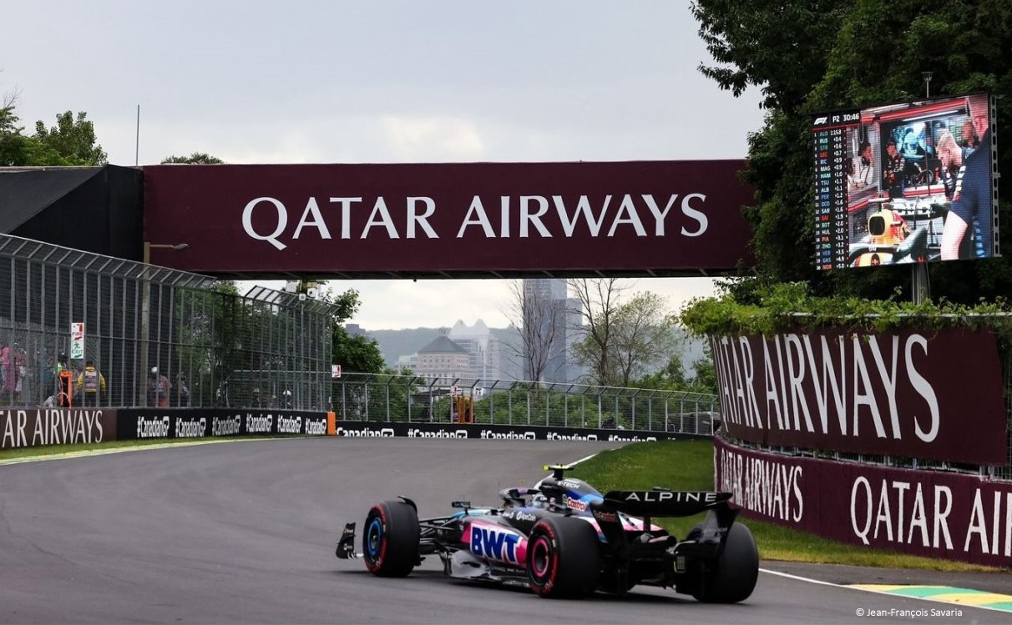 Une voiture de Formule 1 court sur une piste sous une bannière « Qatar Airways », avec des arbres et un horizon de la ville visibles en arrière-plan.