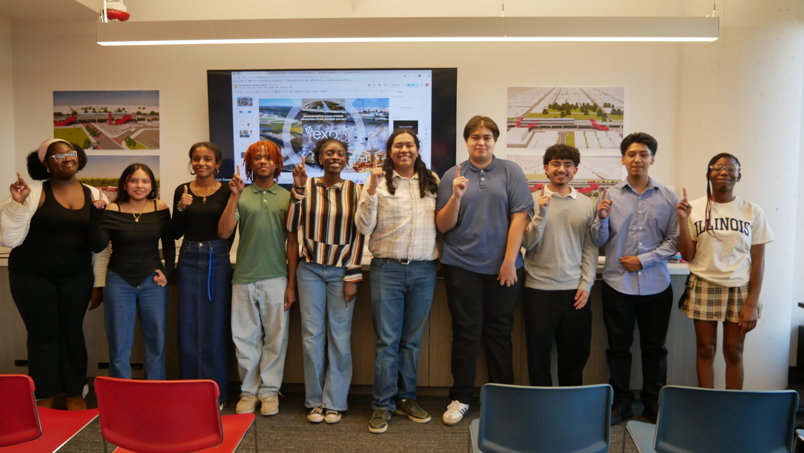Ten Lindblom Math and Science Academy students stand side by side in a classroom, holding up one finger, with a presentation screen and two posters visible behind them.