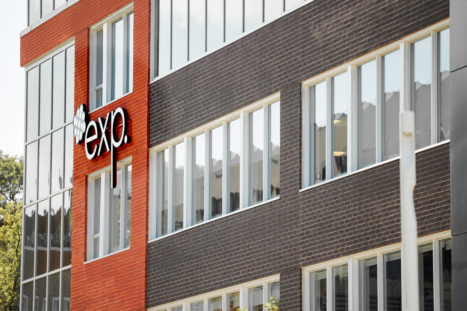 Modern office building with a red and dark brick facade, featuring large windows and a sign reading 