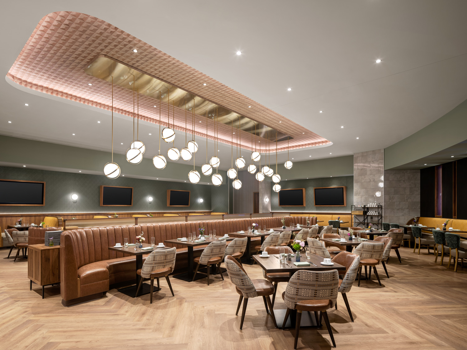 Modern restaurant dining area with wooden flooring, brown leather booths, woven chairs, dark tables, and spherical pendant lights hanging from the ceiling.