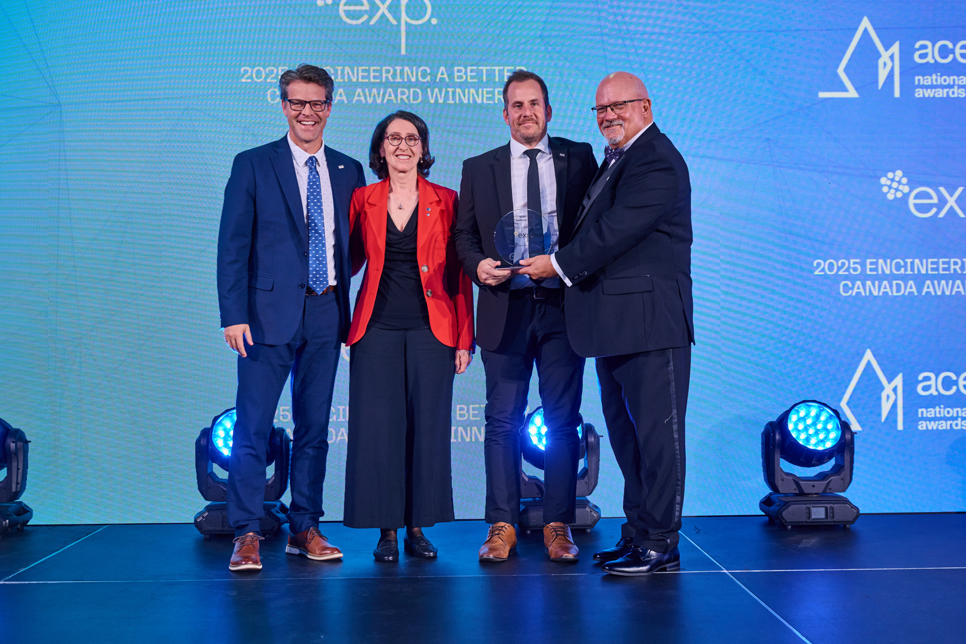 Four people stand on stage, two of them holding an award, with a blue backdrop displaying "2025 Engineering a Better Canada Award Winners" and logos.
