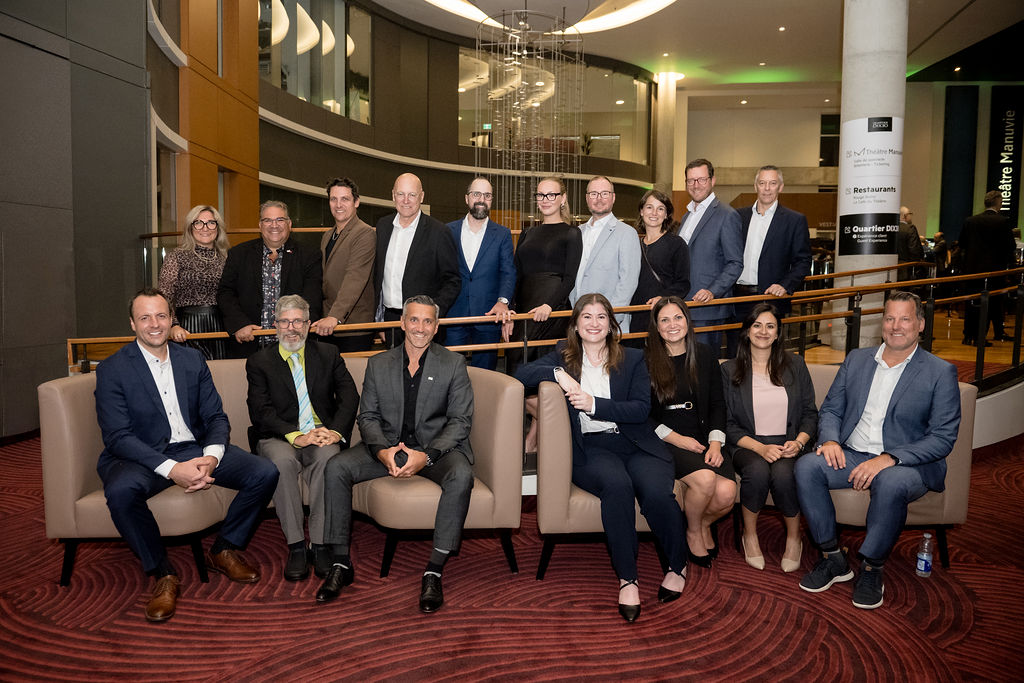 Un groupe de dix-sept personnes, habillées en tenue de travail, pose pour une photo dans un hall d'entrée moderne avec un tapis rouge et une architecture incurvée.