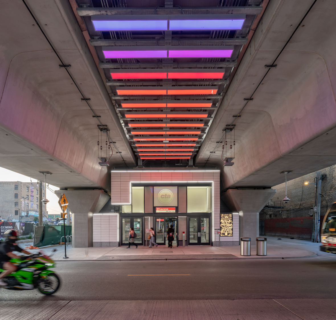 Under a concrete overpass with colored lights, people enter and exit a CTA station while a green motorcycle and a car pass by on the street in front.
