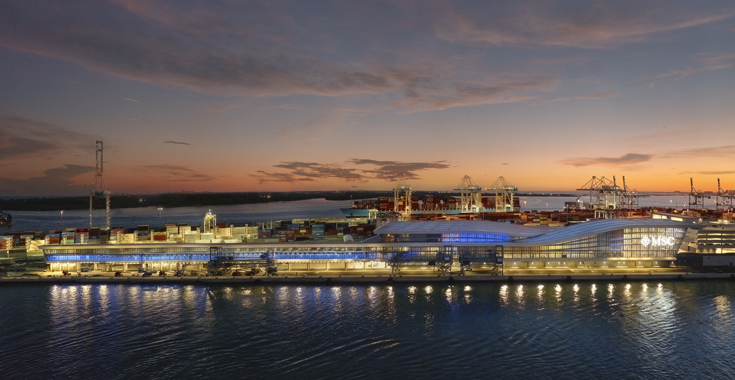 A modern port terminal with MSC signage is illuminated at dusk, with shipping containers and cranes visible in the background by the waterfront.