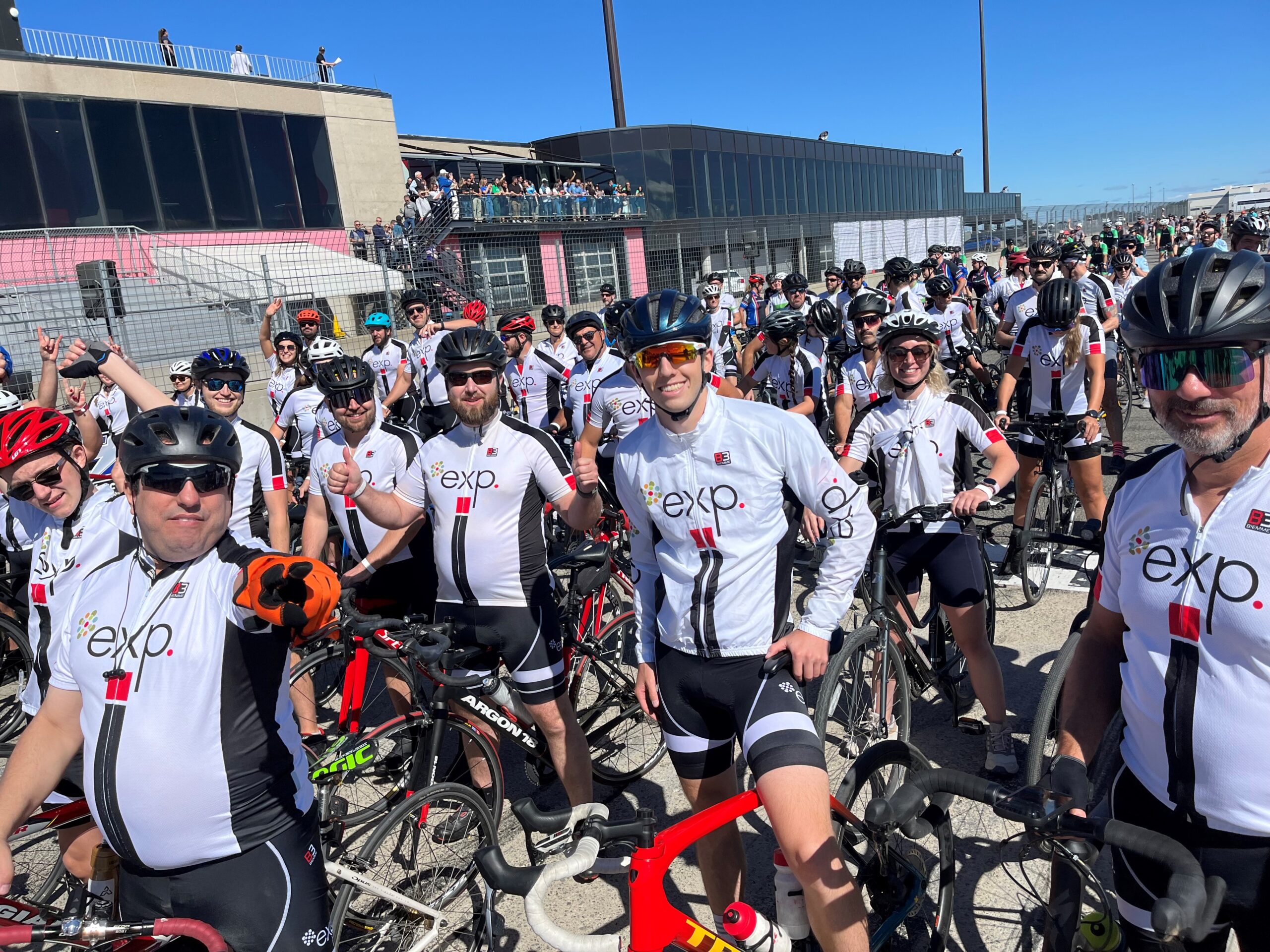 Un grand groupe de cyclistes portant des maillots exp. blancs assortis se rassemblent avec leurs vélos lors d'un événement en plein air par une journée ensoleillée.
