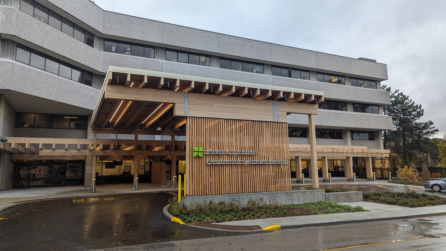 The main entrance of a modern, multi-story hospital building with a wooden canopy and a sign reading 