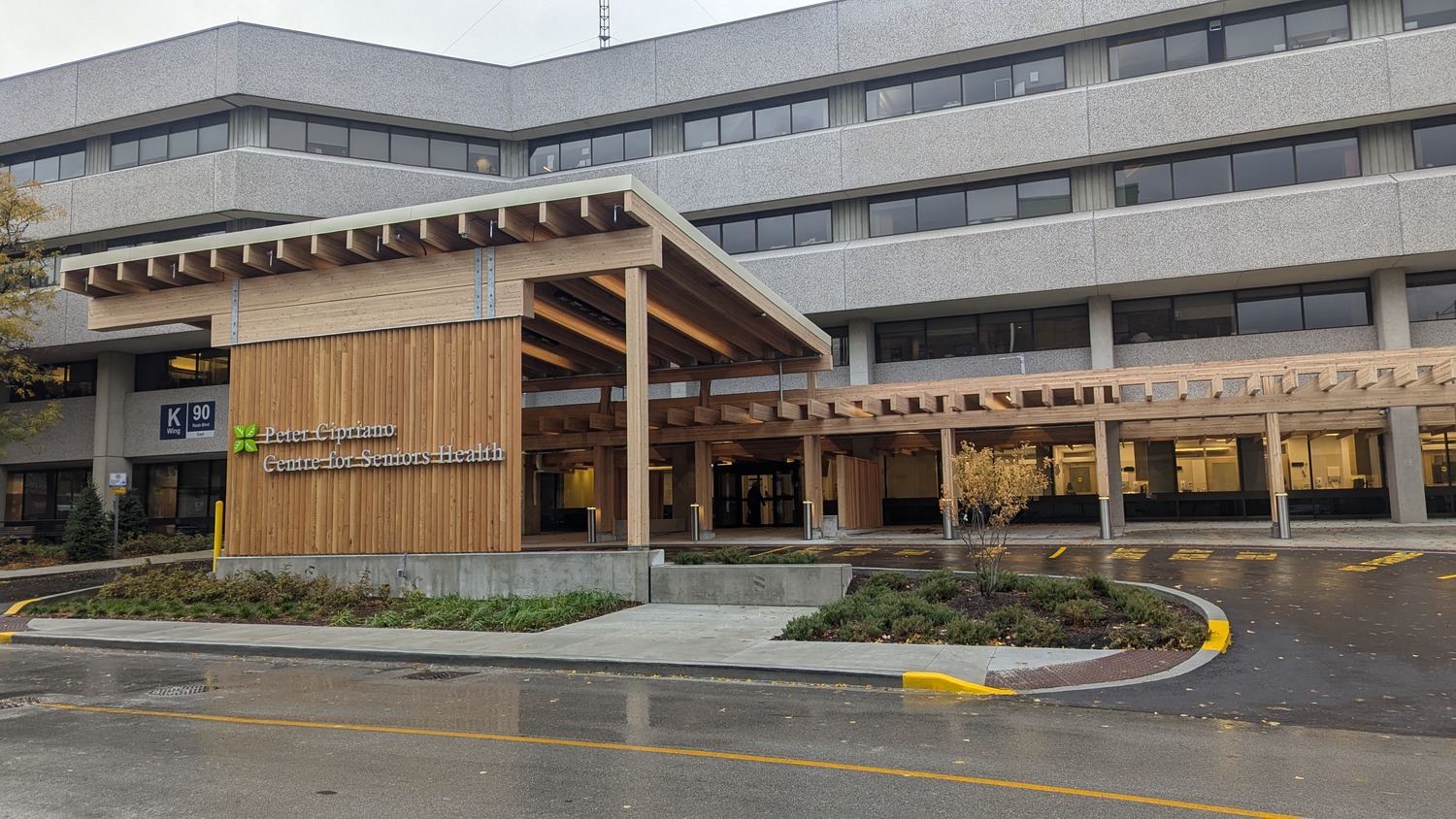 Exterior view of a modern medical center entrance with a wooden canopy, glass doors, and a sign reading “Interior Community Services - Centre for Diversion and Health.”.