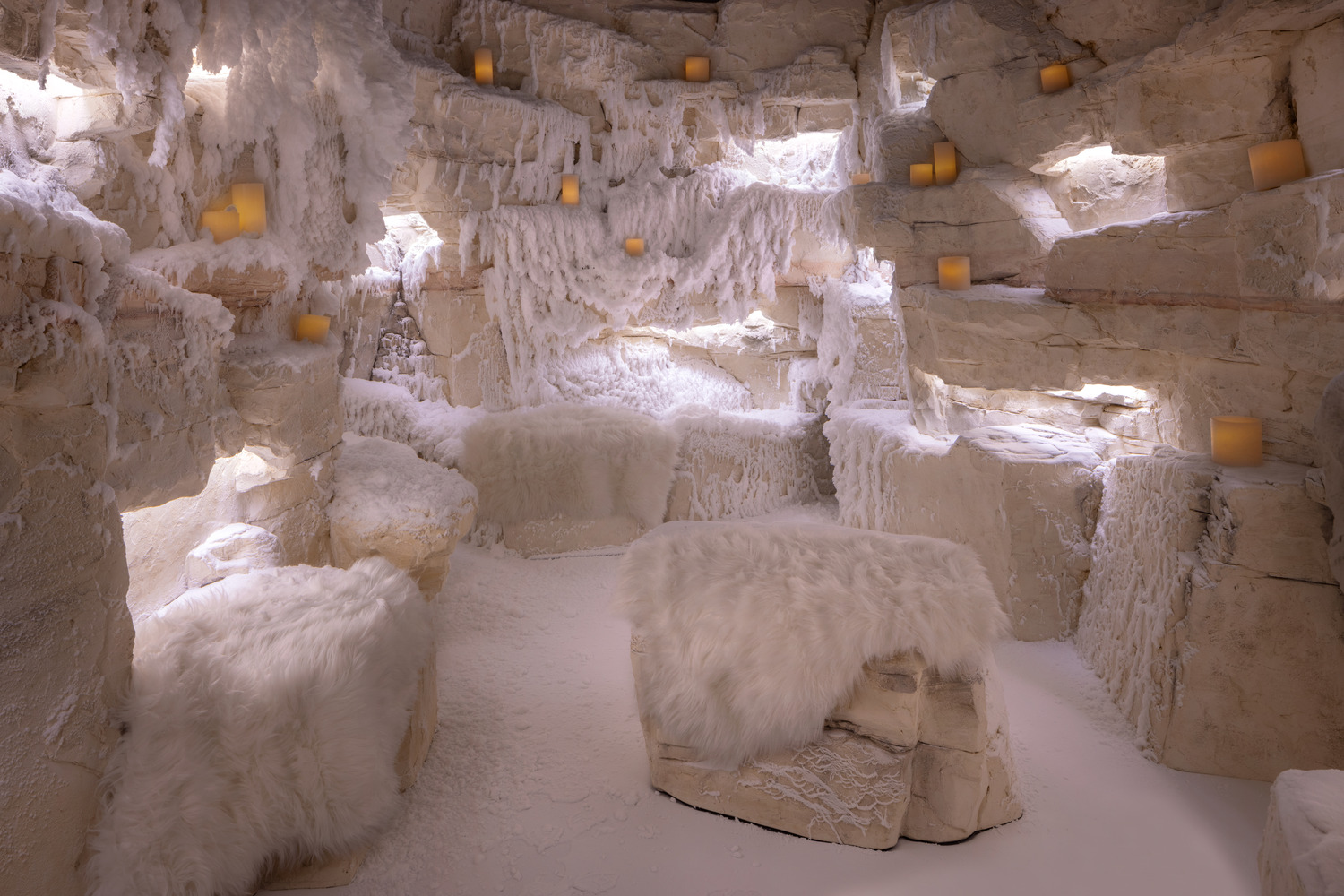 Une salle aux murs de pierre et aux bancs recouverts de fausse fourrure blanche, décorée de bougies et de neige artificielle, créant une atmosphère hivernale de grotte.