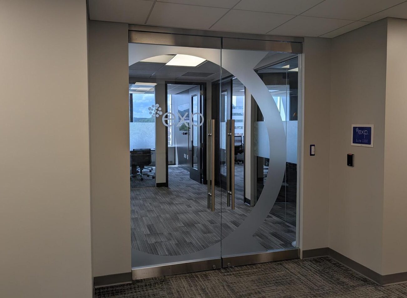 Glass double doors with a circular design lead to an office conference room, featuring carpeted floors and glass walls with a frosted pattern.