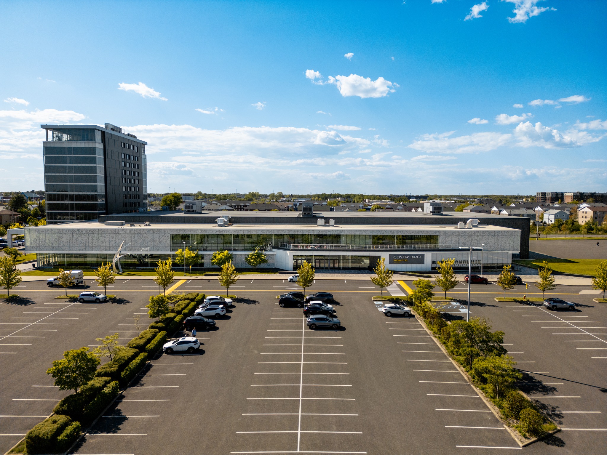 A modern office building with a mostly empty parking lot under a blue sky with scattered clouds.