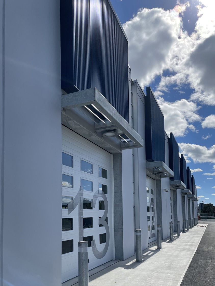 Row of modern industrial garage doors, each labeled with large numbers, under a partly cloudy sky with sunlight casting shadows on the ground.