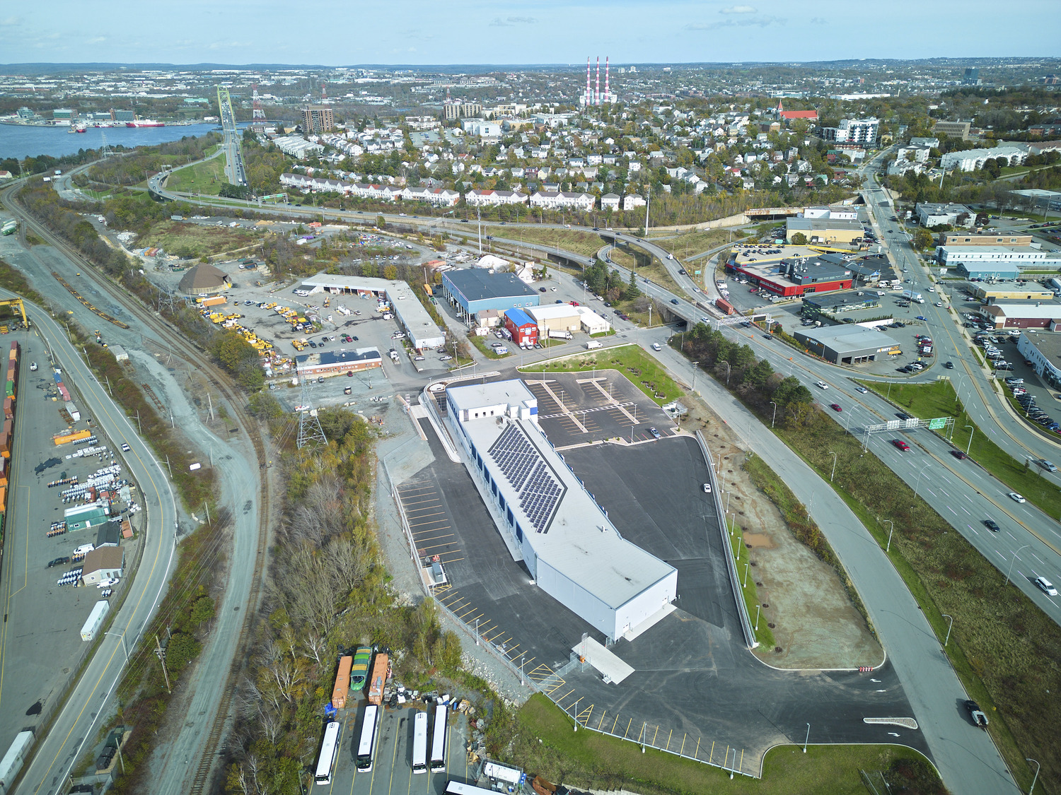 Aerial view of a commercial area with a large white building in the center, surrounding parking lots, roads, and a residential neighborhood in the background.