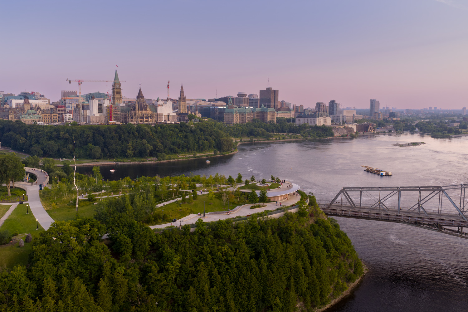 Aerial view of Ottawa city skyline with Parliament Hill, trees, Ottawa River, Alexandra Bridge, and a glowing sunset sky resembling a constellation.