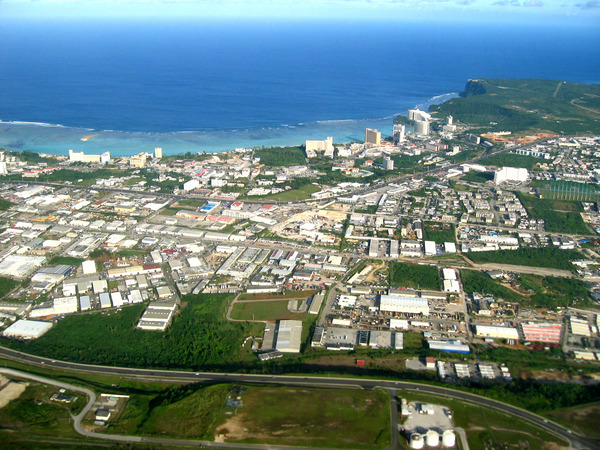 Aerial view of a coastal city with dense buildings, nearby highways, and the ocean in the background under a clear sky.