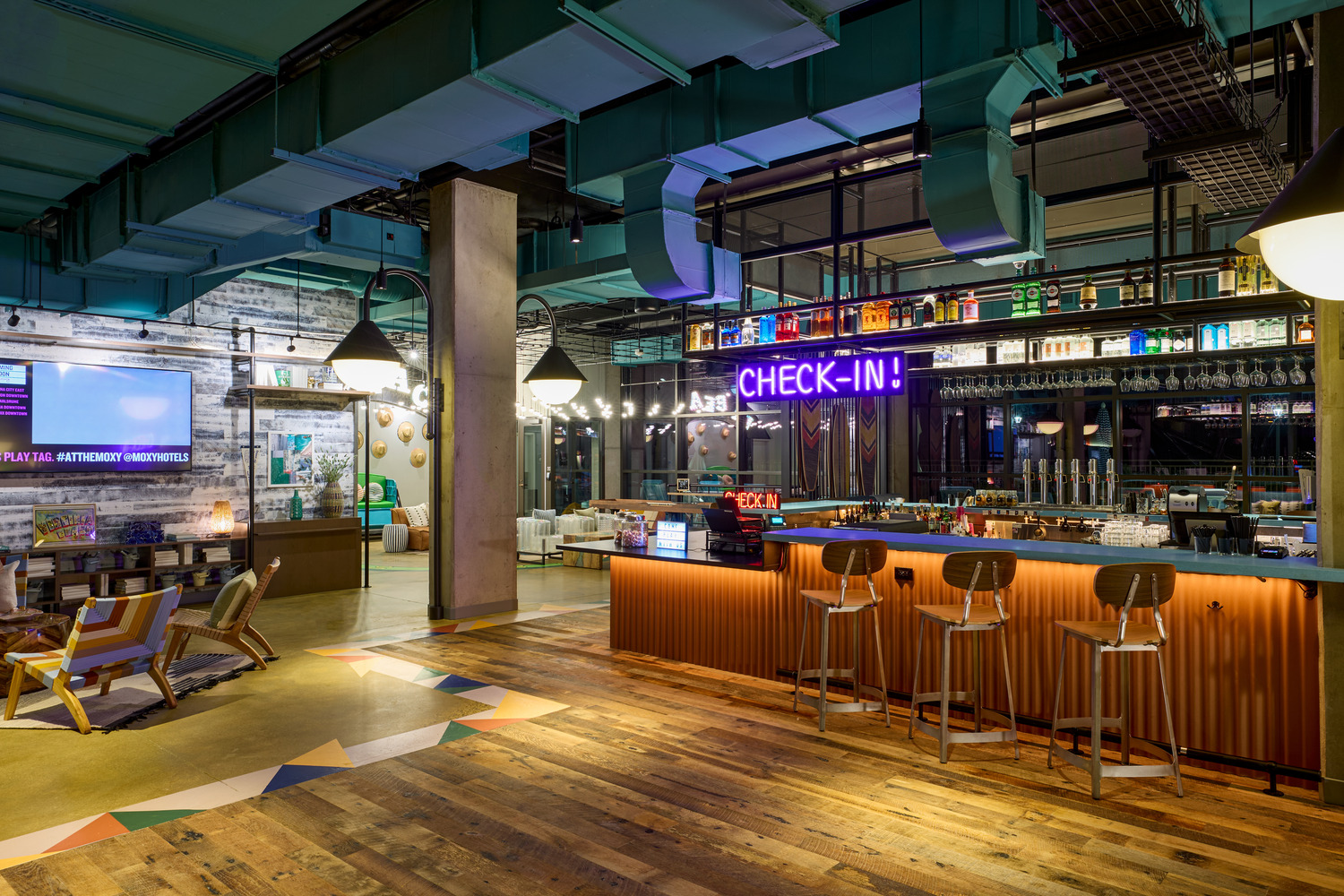 Lobby area featuring a check-in counter with neon sign, bar stools, wooden flooring, modern lighting, and eclectic décor.