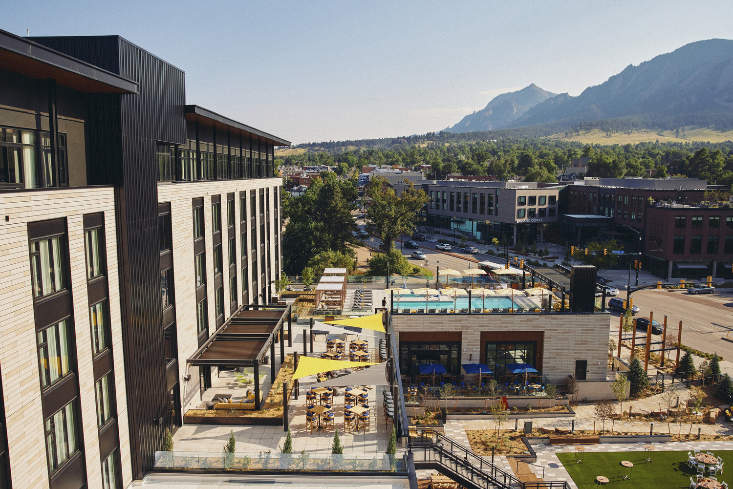 Experience Limelight Boulder: a modern hotel with outdoor seating, a pool area, and stunning mountain views, all nestled in a suburban setting under a clear sky.