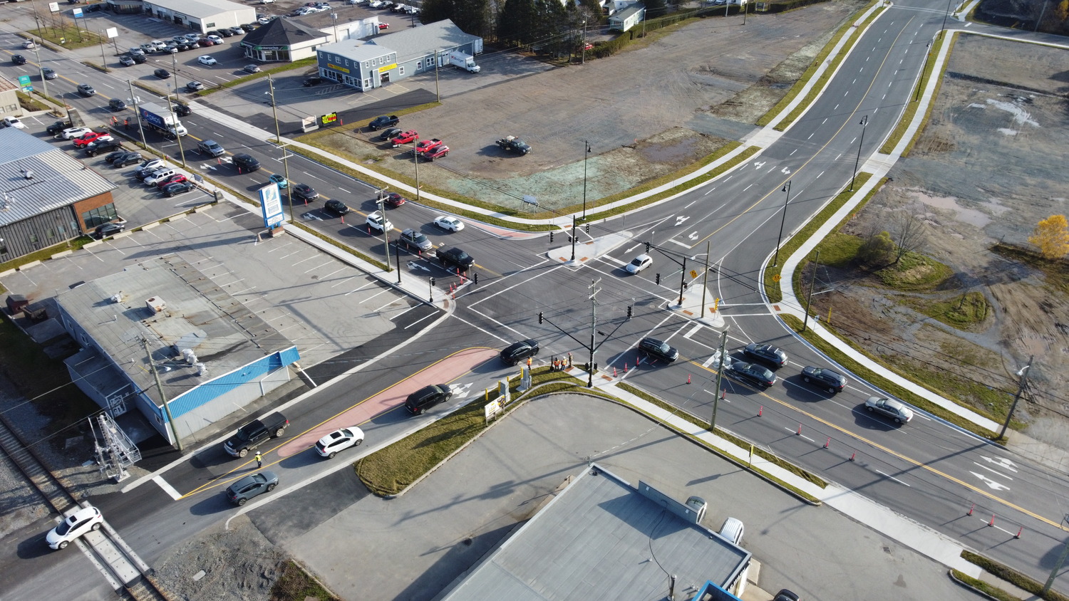Aerial view of a busy urban intersection with multiple cars waiting at traffic lights near commercial buildings and parking lots.