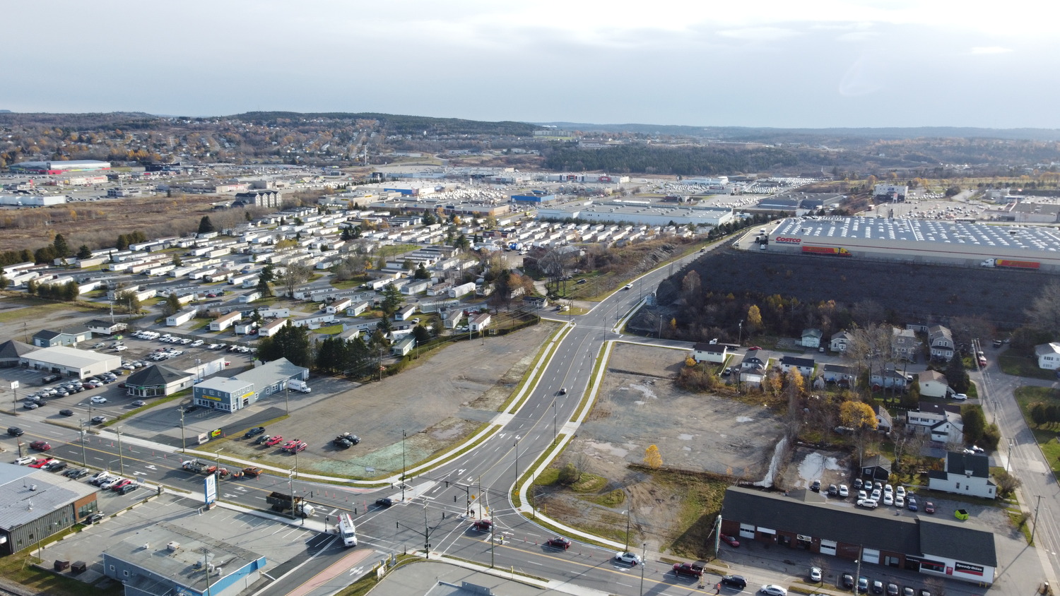 Aerial view of an urban area featuring commercial buildings, a large warehouse, mobile homes, residential houses, and several intersecting roads.