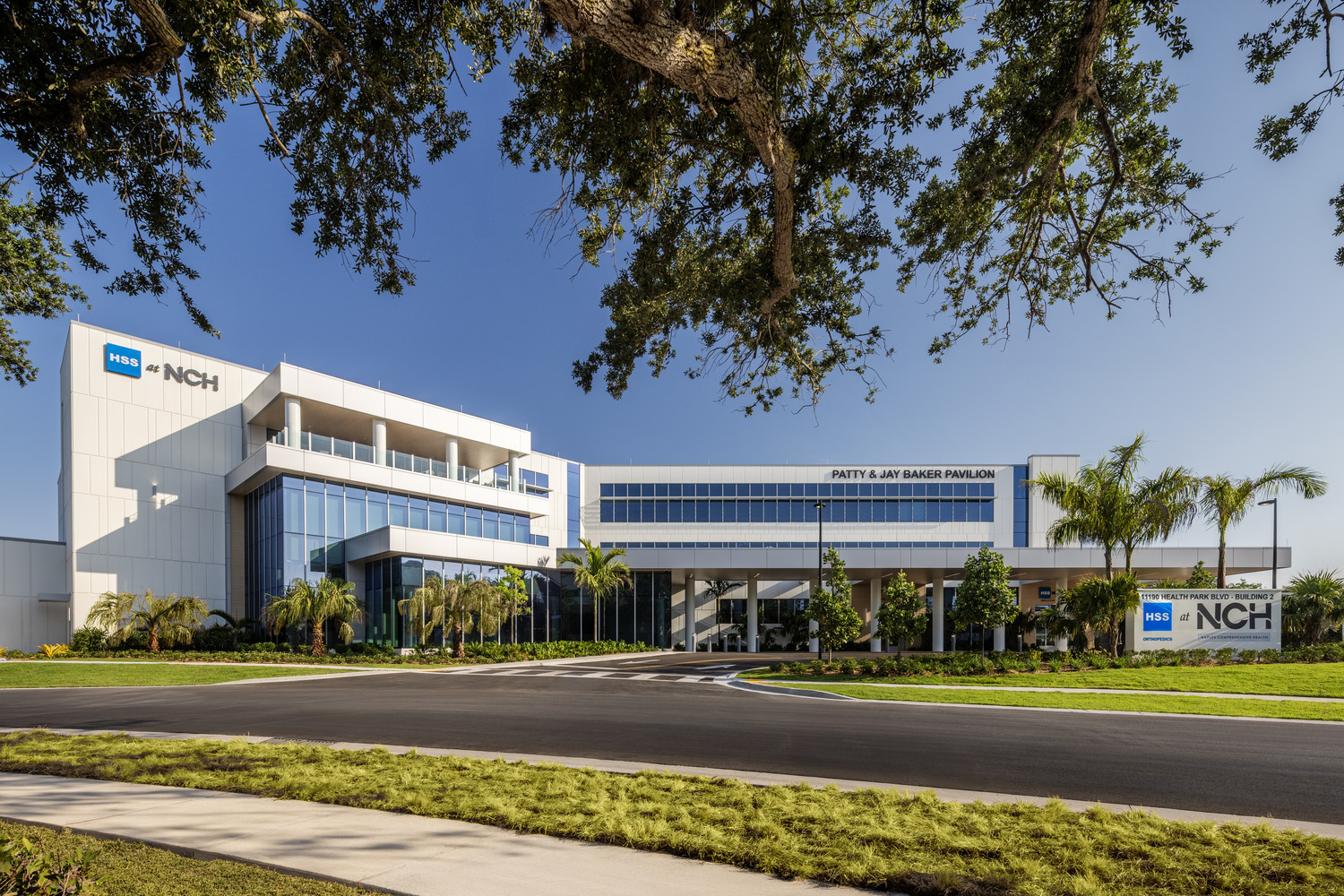Modern hospital building with glass windows, palm trees, and a sign reading "NCH" and "Patty & Jay Baker Pavilion" on a clear day.