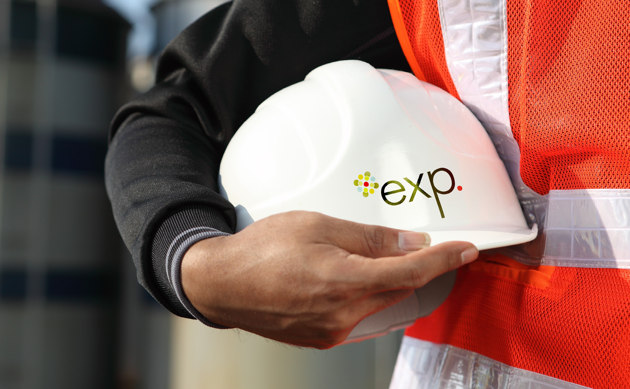 Une personne portant un gilet de sécurité orange tient un casque blanc portant l'inscription "exp.