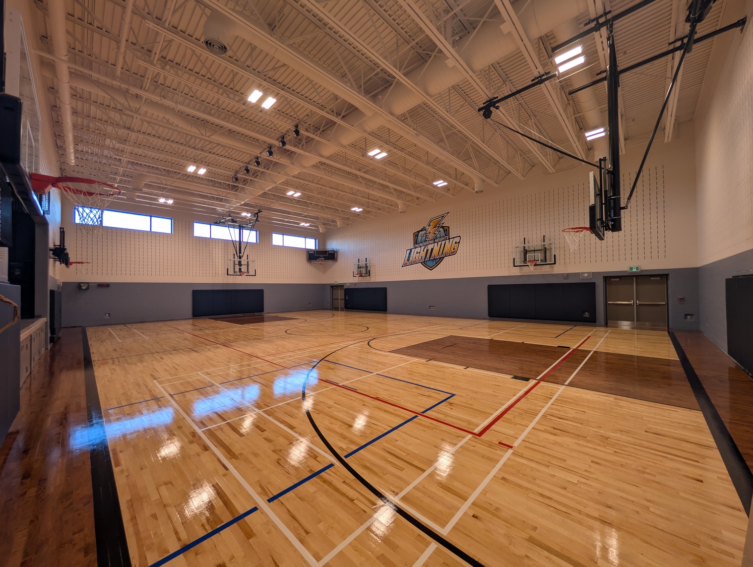 Wide-angle view of an empty indoor basketball court with polished wooden flooring, basketball hoops, and a 