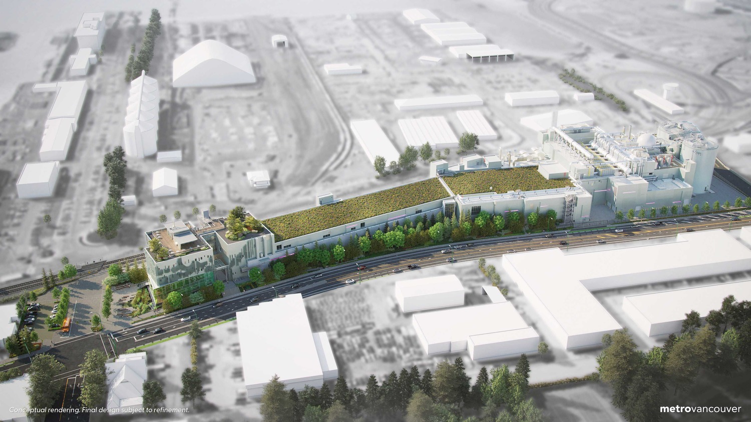 Aerial view of a large industrial facility with green rooftops, surrounded by trees and roads, set in an urban area with several nearby buildings.
