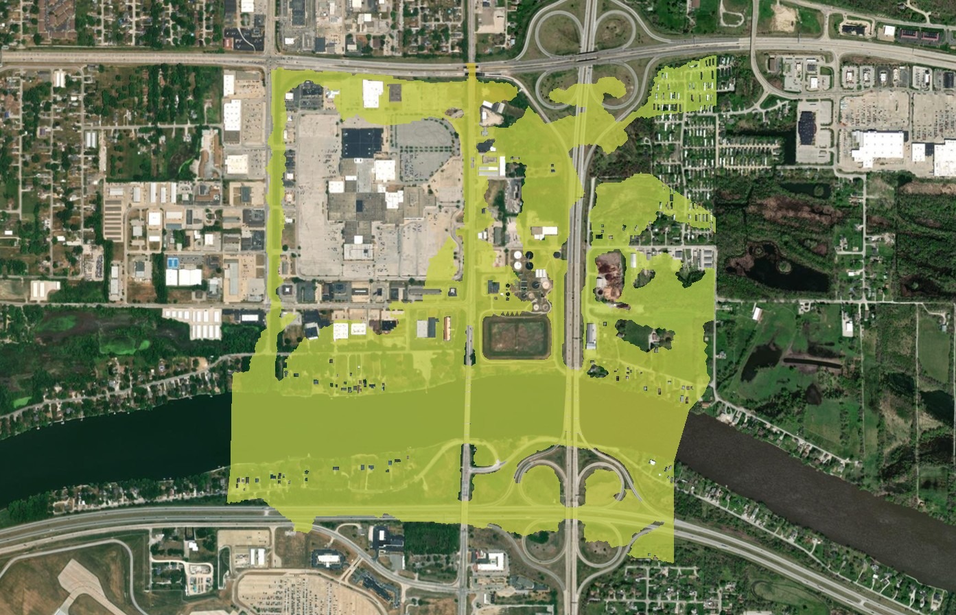 Aerial view of an urban area with highways, shopping centers, and residential zones; a large semi-transparent yellow overlay highlights a specific section, emphasizing the application of hydraulic modeling for flood risk assessment in that area.