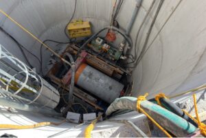 A cylindrical pipe segment and industrial equipment at the bottom of a concrete maintenance shaft.