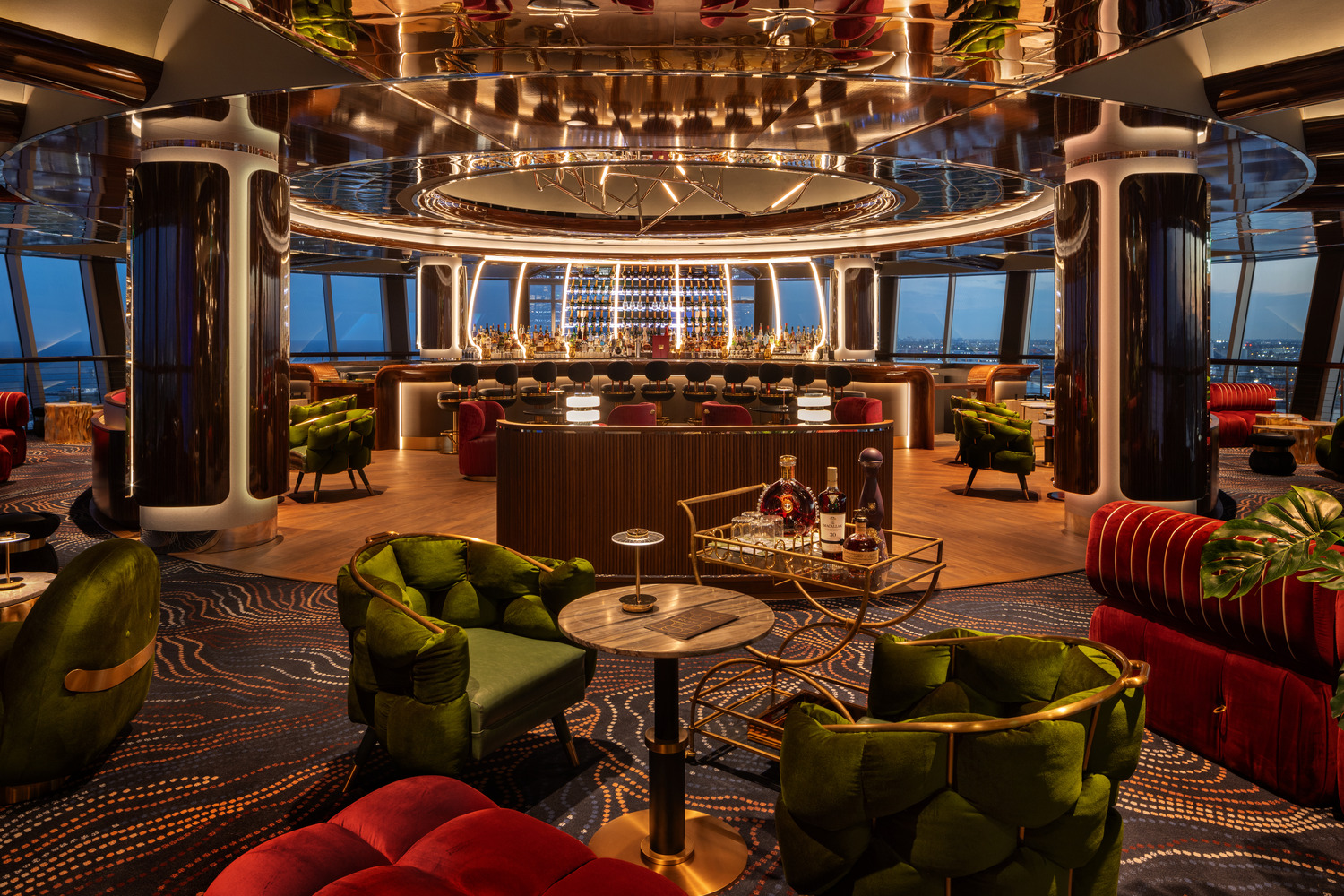 Modern lounge with an illumination award design, featuring a central bar, velvet green armchairs, round tables, and city skyline views through floor-to-ceiling windows.