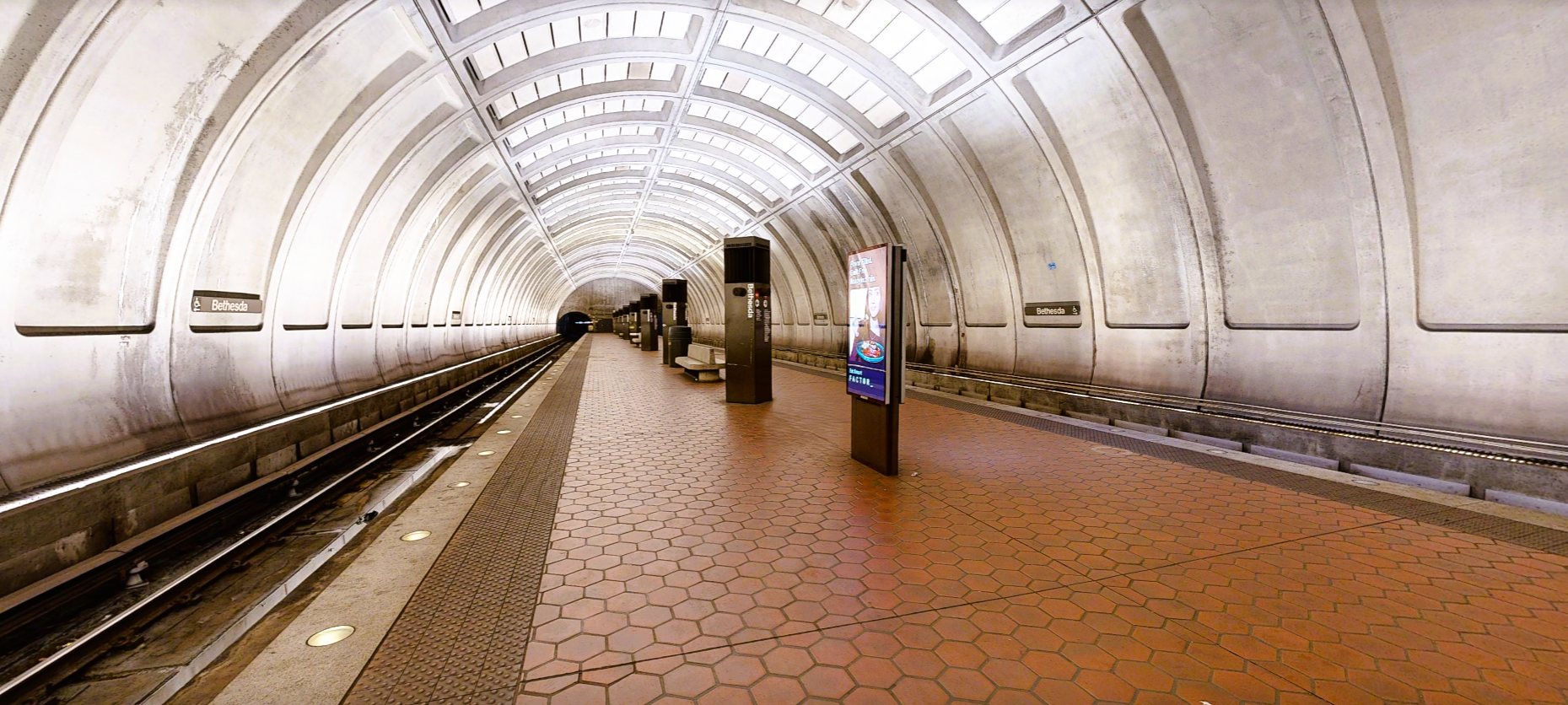 The empty Bethesda Metro station platform with a vaulted concrete ceiling and hexagonal red floor tiles.